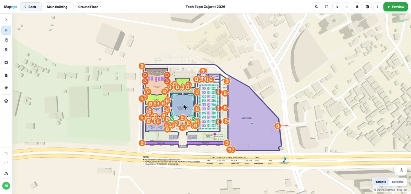 The Mapnyx Studio editor: an exhibition venue drawn over its real site with hall and booth polygons, colour-coded zones, walkways, a parking boundary and a pin on every point of interest, with the drawing toolbar down the left and a streets or satellite basemap toggle.